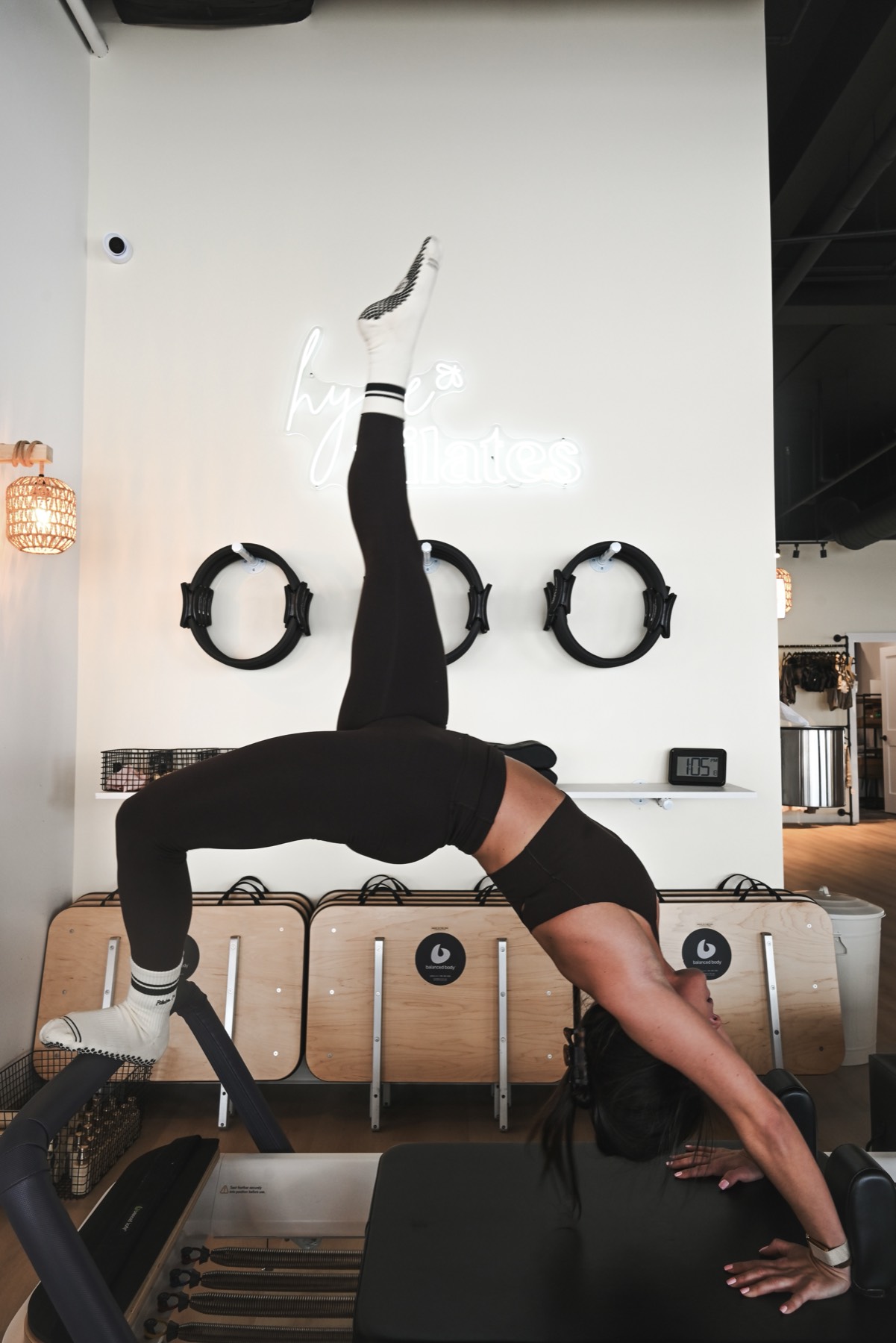 A member in a bridge pose on the reformer beneath the Hyve Pilates neon sign